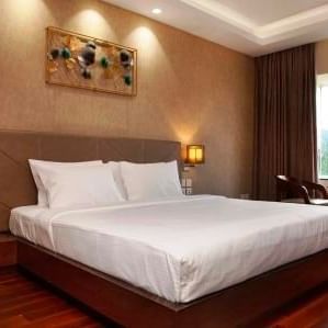 A double bedroom with sockets near the bed, two lamps on either sides of the bed, and a seating area near the glass window at The Hamuse Hotel, Kodaikanal