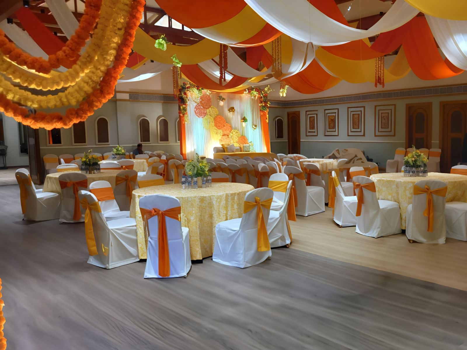 A well decorated event hall at Vedic Village Spa Resort with floral garlands featuring  cluster style seating arrangements.