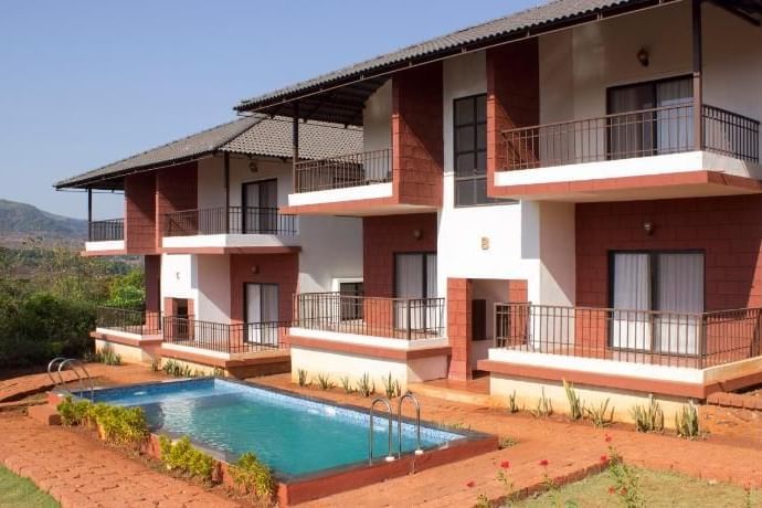 The facade of Forest Greens resort featuring two storeys, an outdoor swimming pool, and a view of the expansive landscape in the background.