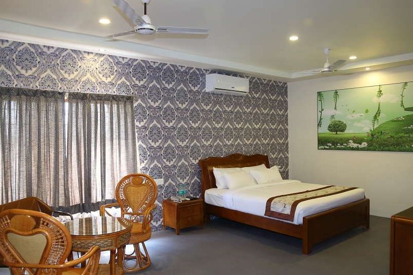 Themed Villas of GK Hill View Resort furnished with a double bed, wall-mounted AC, a chair and curtained windows.