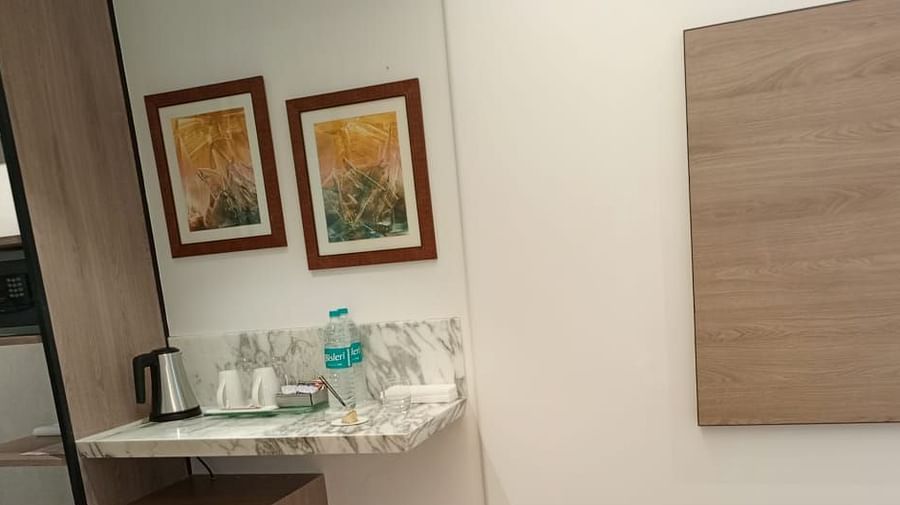 A wooden wardrobe area of an executive room in Mirage Hotel, featuring a kettle and a tray of refreshments, placed on a marble counter top with wall decor in the backdrop.