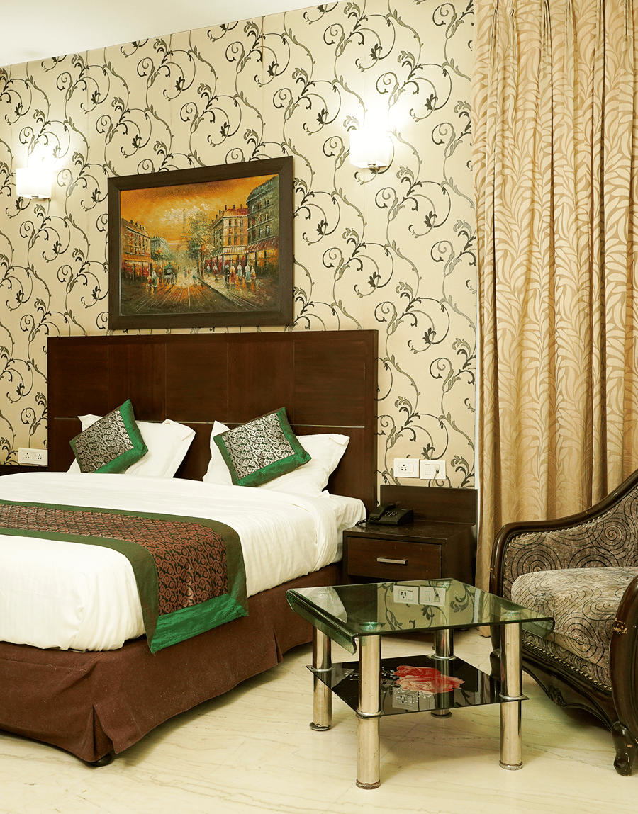King bed, carved armchair and glass side table in the Deluxe Room with Balcony at Lime Tree Hotel, IFFCO Chowk