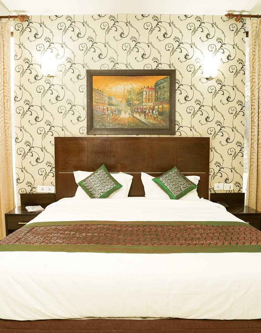 King bed with green cushions below a framed painting in the Deluxe Room with Balcony at Lime Tree Hotel, IFFCO Chowk