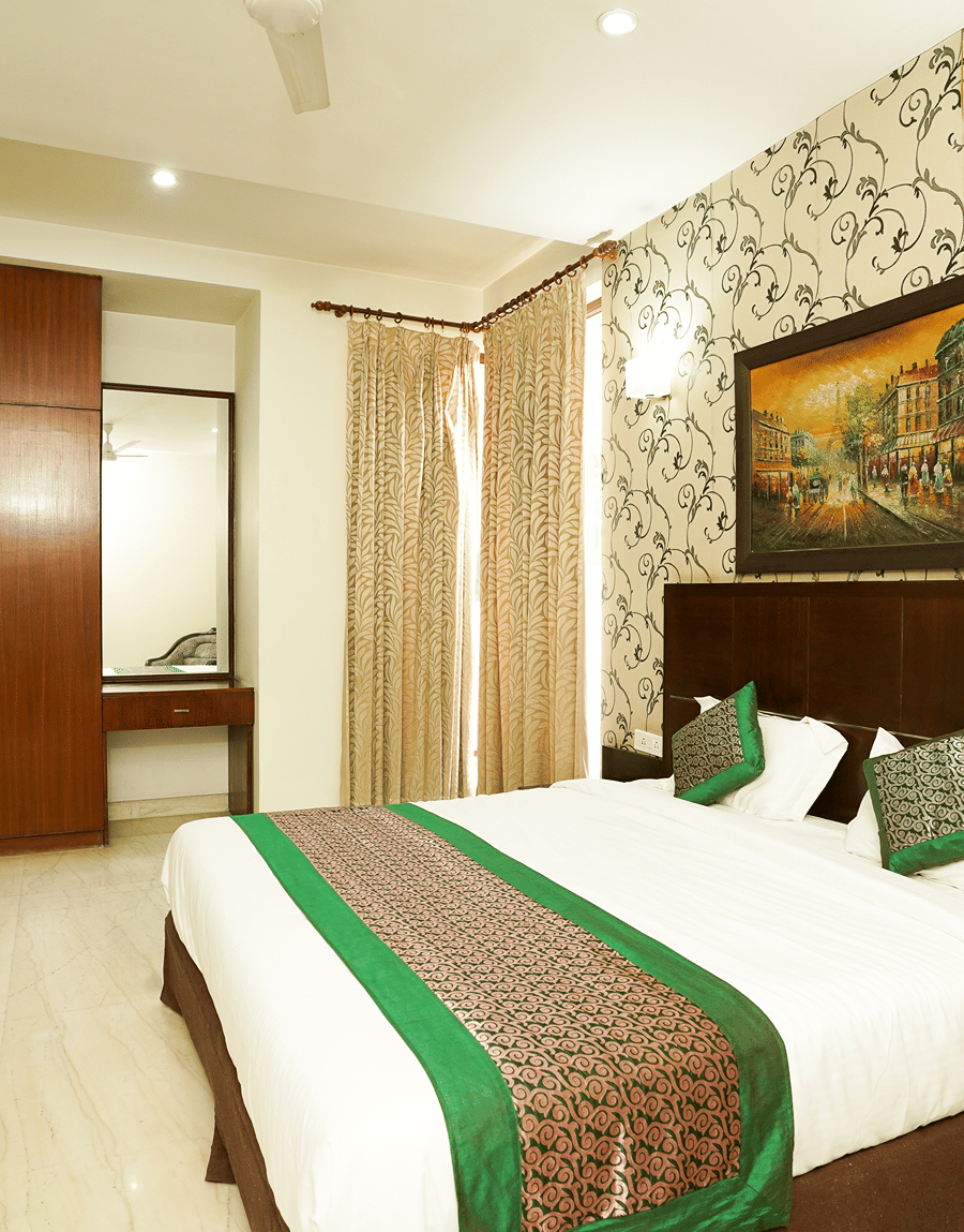 King bed with a green runner, gold curtains and a mirror in the Deluxe Room at Lime Tree Hotel, IFFCO Chowk