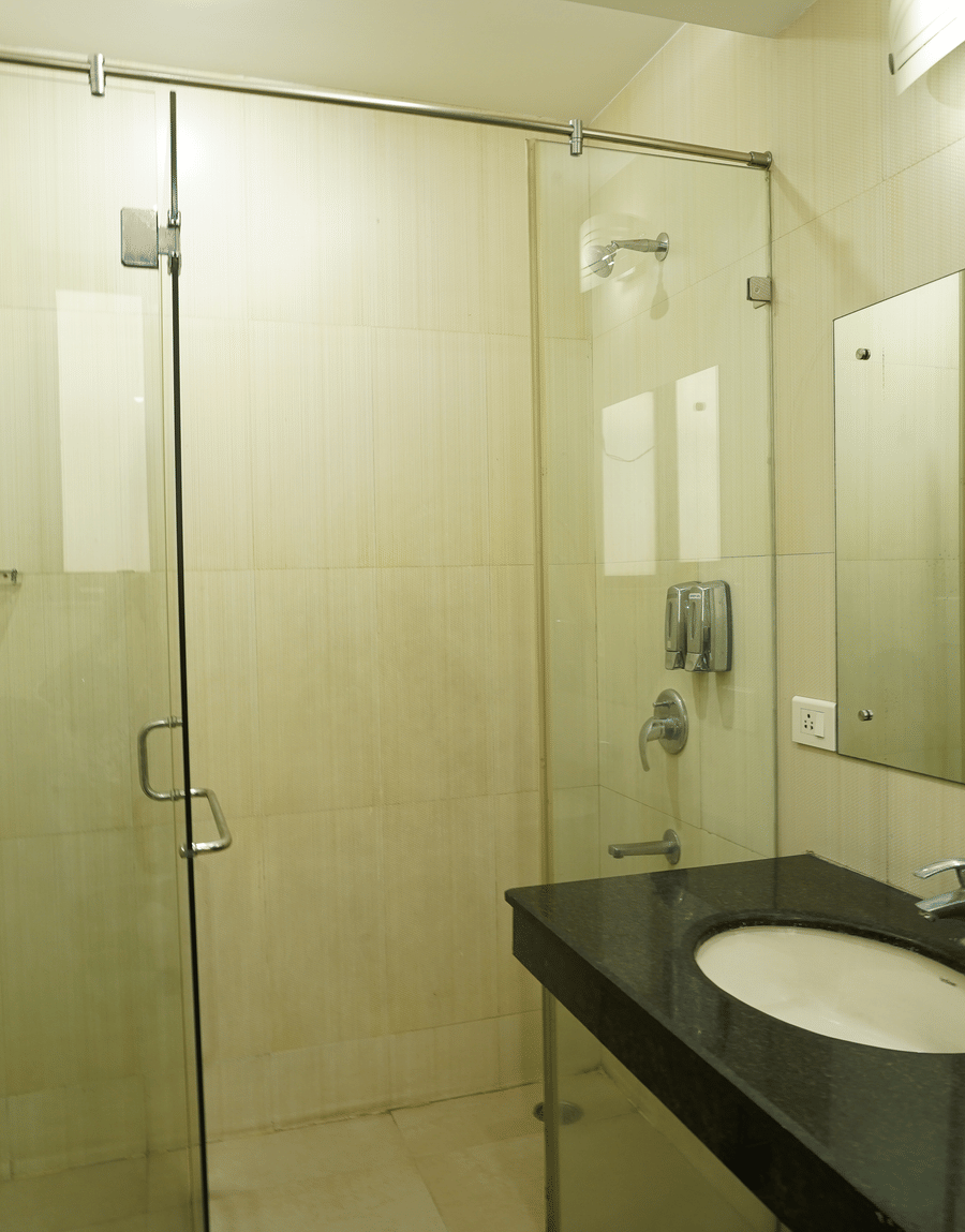 Glass-walled shower and a black vanity with washbasin in the Deluxe Room bathroom at Lime Tree Hotel, IFFCO Chowk