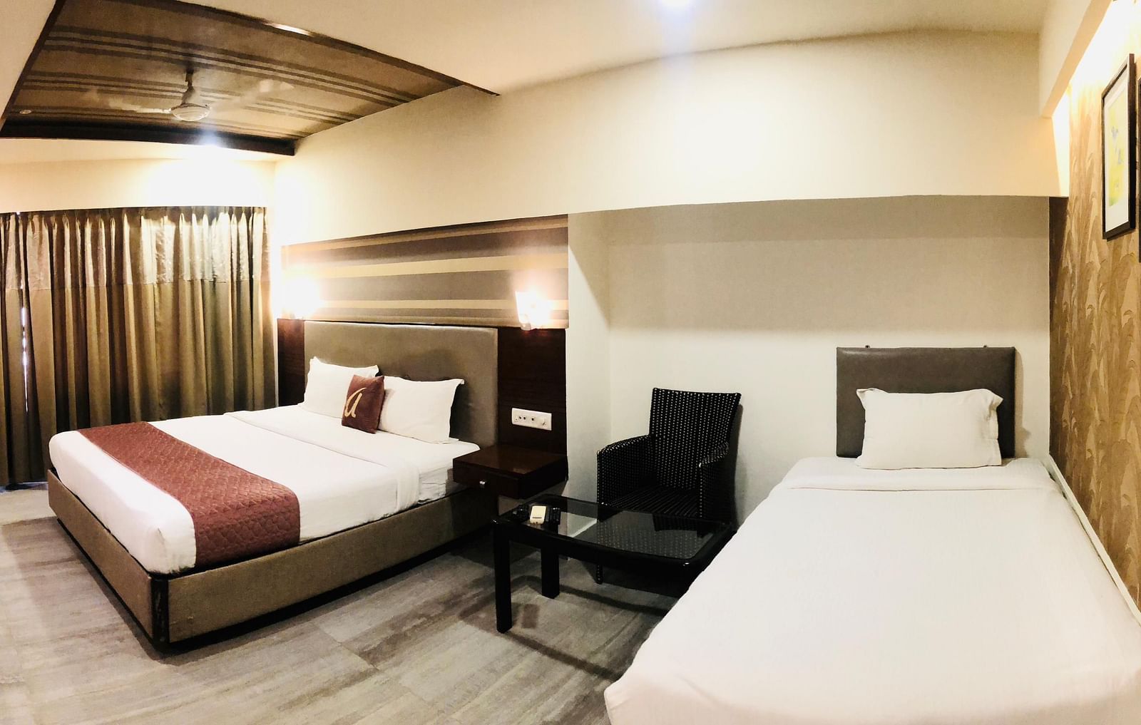 Hotel room featuring a double bed with a maroon runner, a twin bed with white linens, a sofa, and a visible portion of a work desk  | Astra Hotels and Suites Kadubeesanahalli