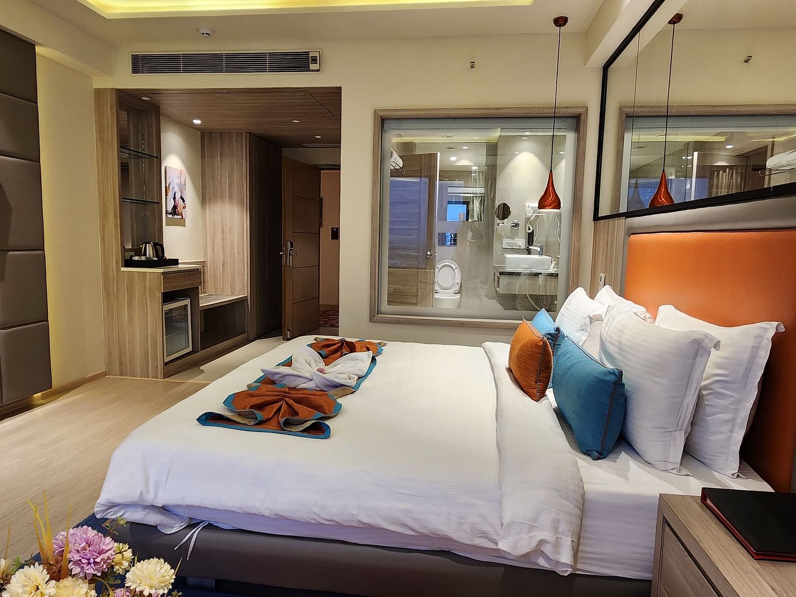 Stylish hotel room with a king-sized bed, colourful cushions, and a glass wall separating the bathroom.