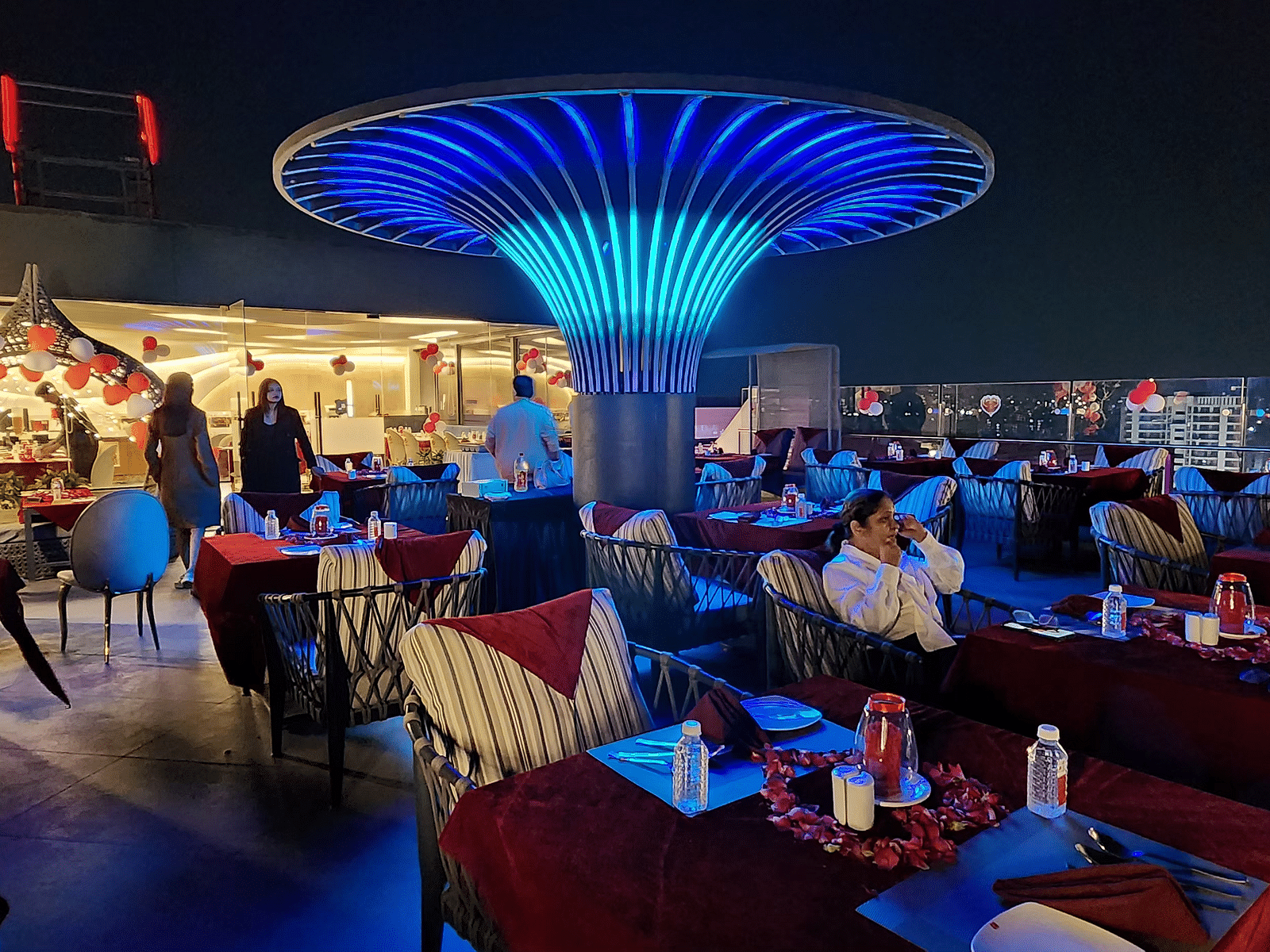 A vibrant restaurant interior with modern blue lighting and red chairs, featuring a central decorative light fixture shaped like a mushroom.