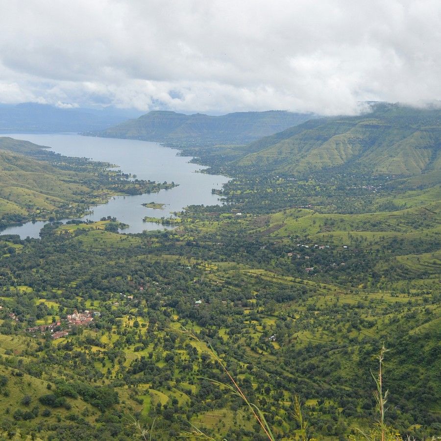 A sweeping view of a verdant landscape with rolling hills and a distant lake, under a cloudy sky.