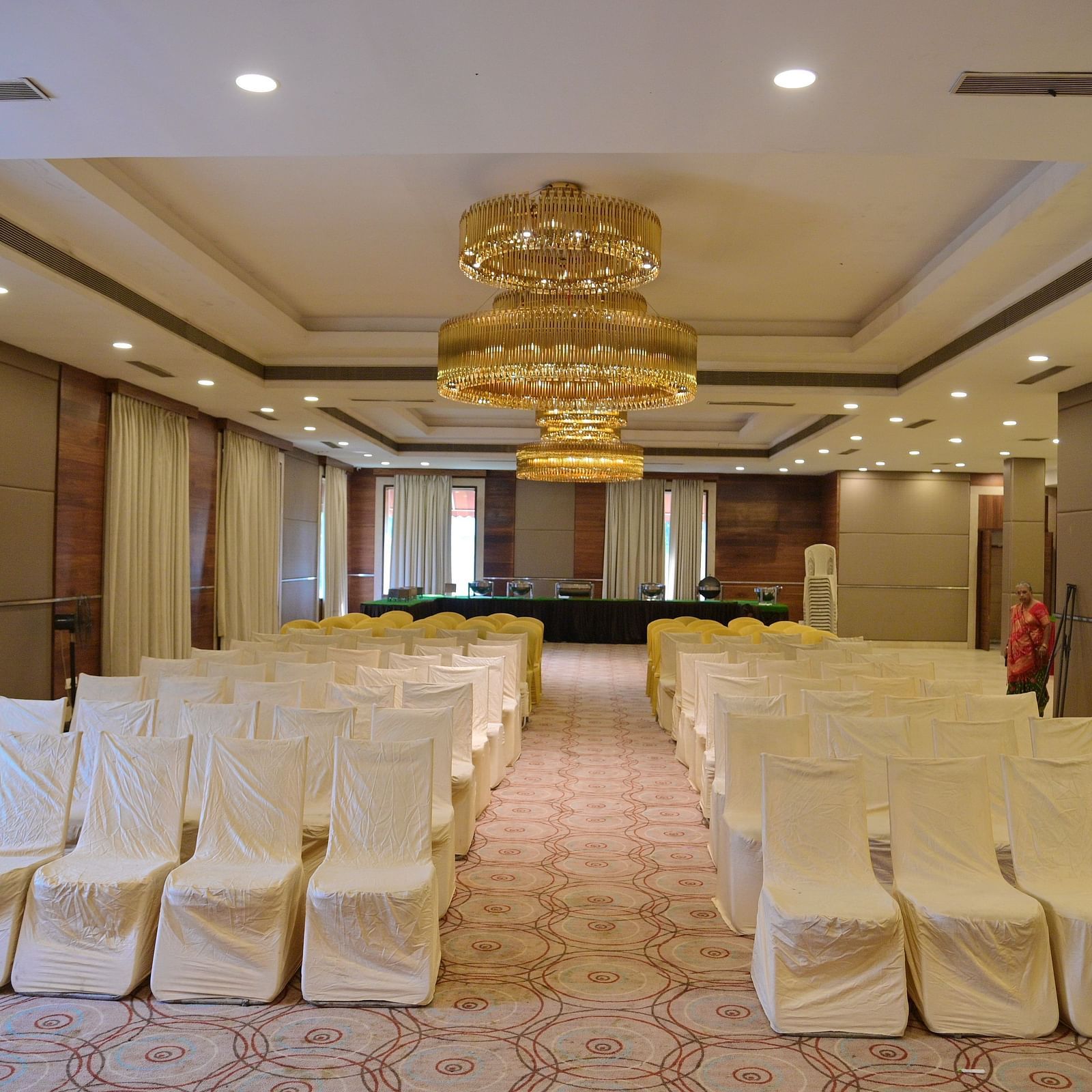Banquet hall with rows of white chairs arranged in theatre style, lit by a chandelier above at Rang Lords Inn Bharuch