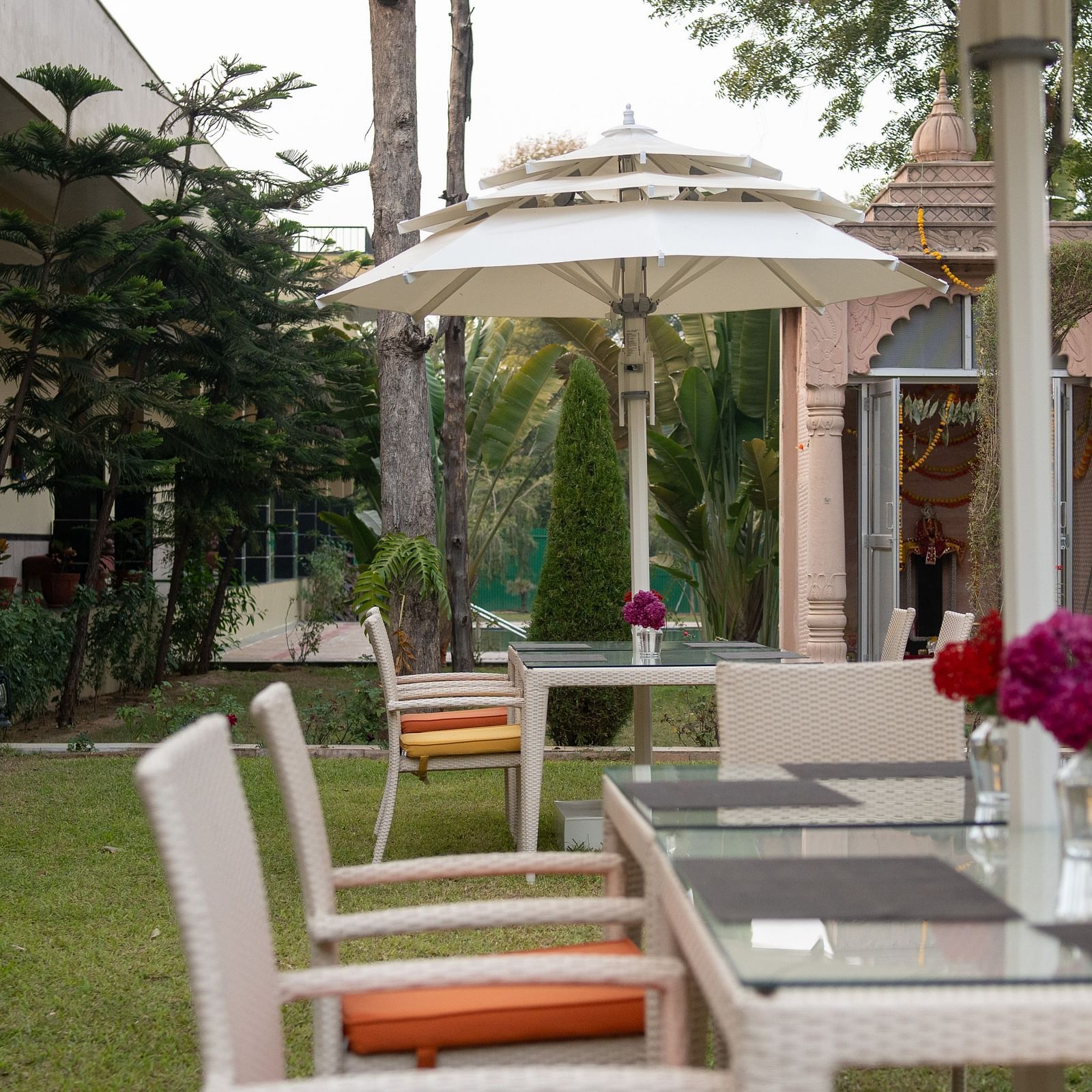 An outdoor dining area at Aamaghati Jungle Retreat Ranthambore with white tables chairs and umbrellas.