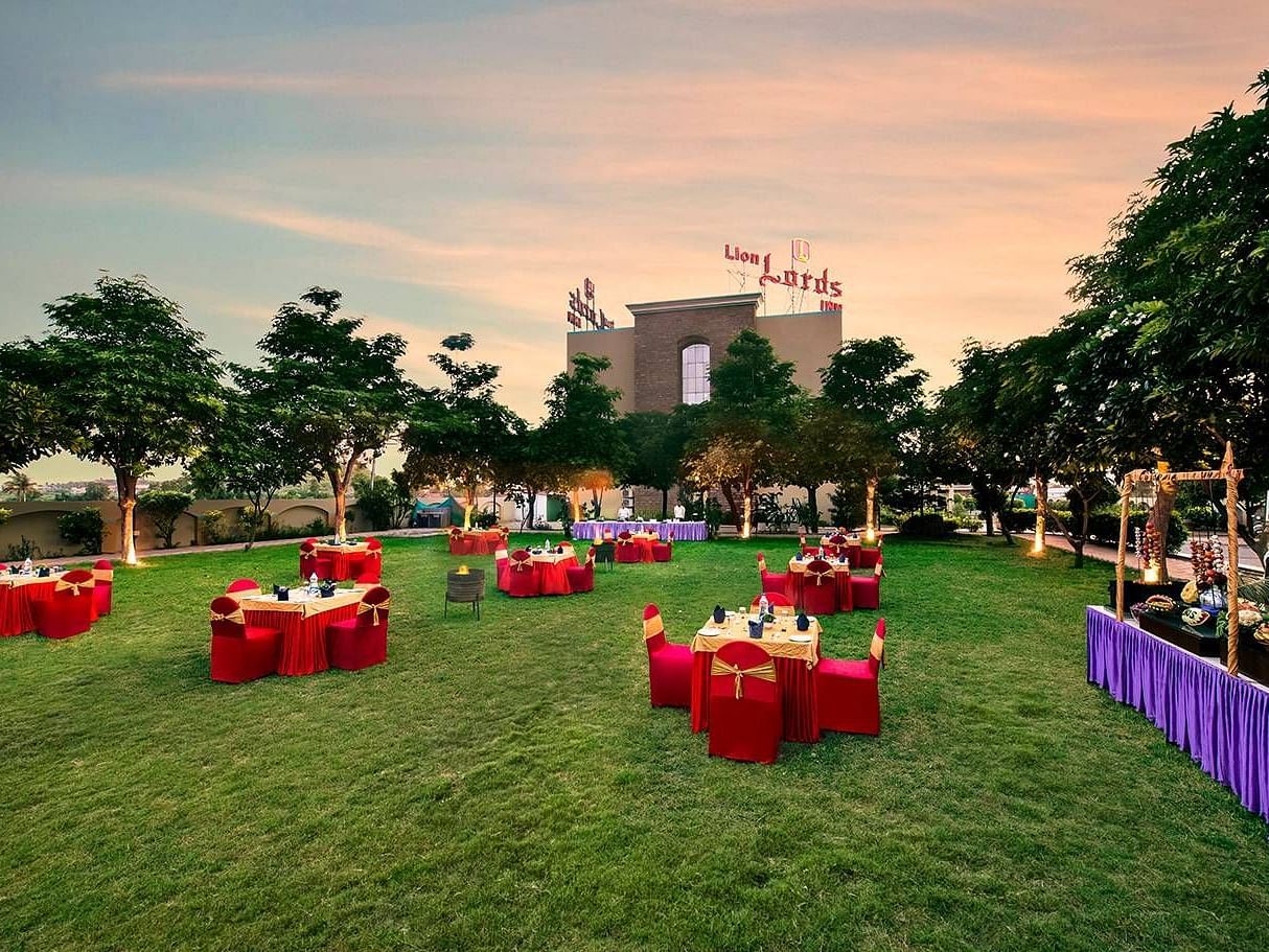 An outdoor area is prepared for an event with tables covered in red cloths on the grass - Lion Lords Inn Rajula