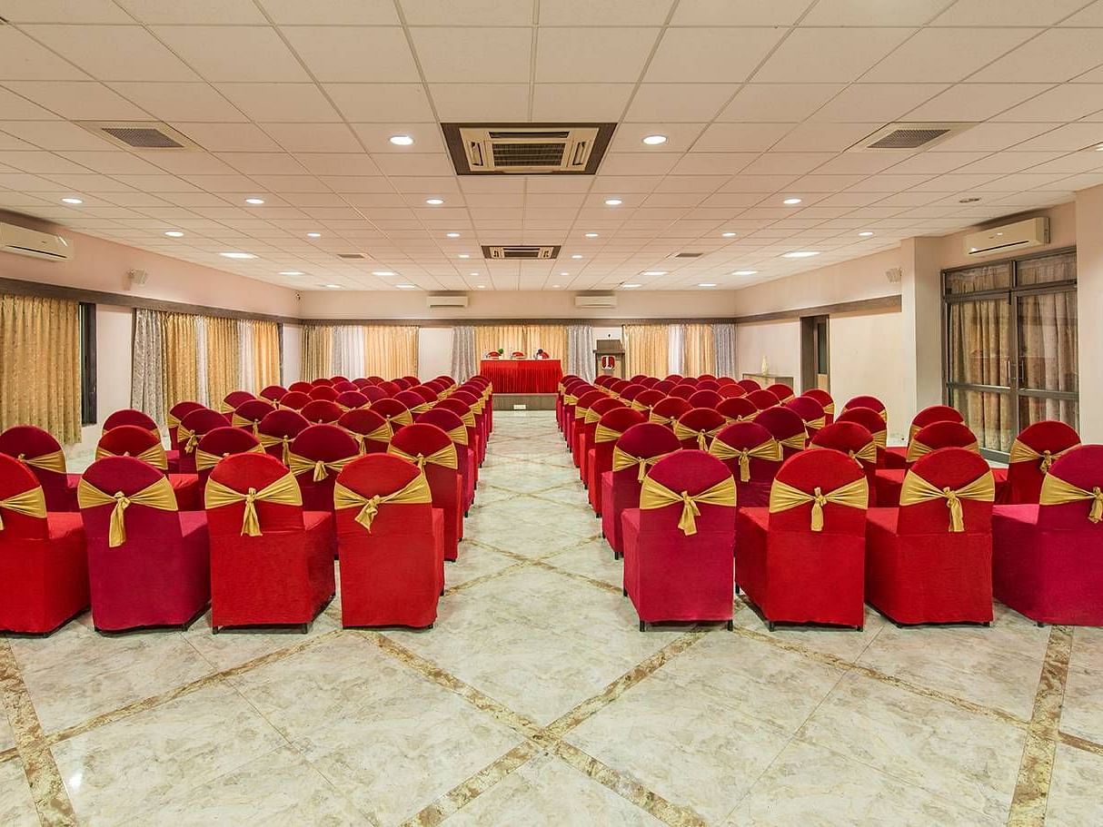 A large hall is set up with rows of chairs covered in red fabric for an event - Lion Lords Inn Rajula