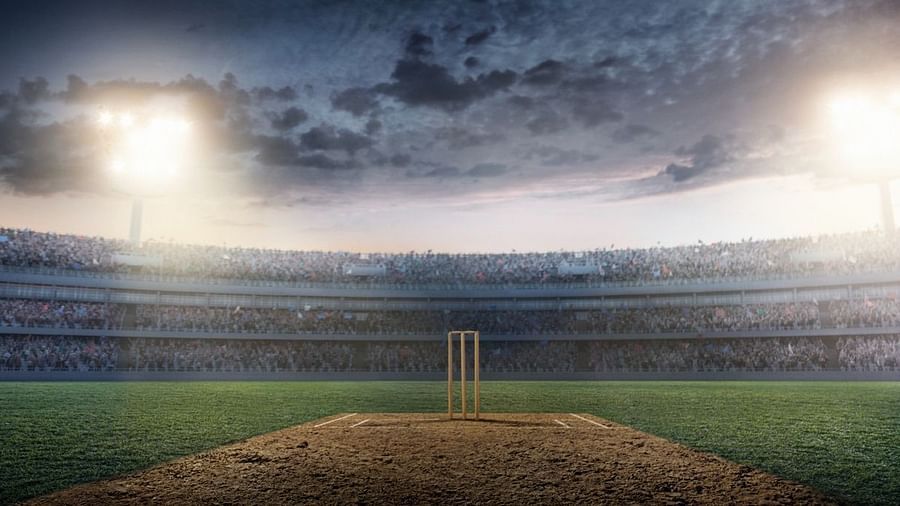 Night view of a cricket stadium with the wicket and bails in the center, surrounded by a large, filled crowd, and a dramatic sky overhead