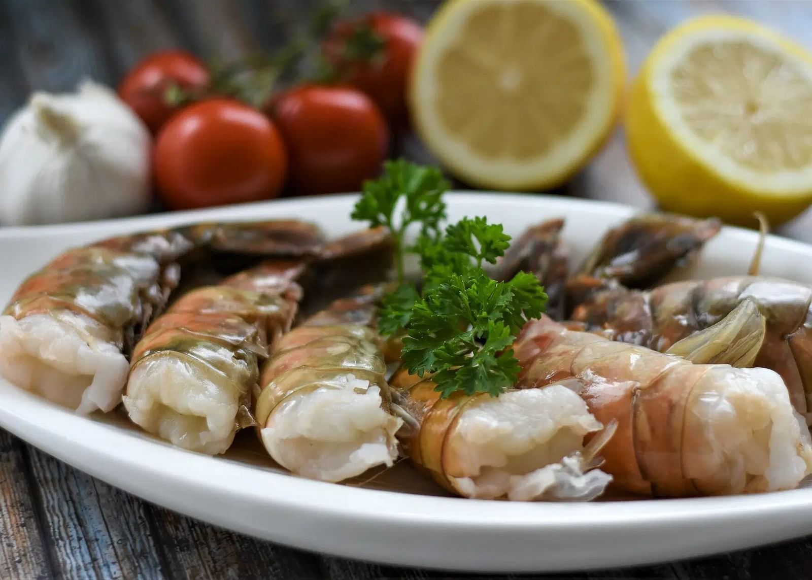 A plate of cooked shrimp garnished with parsley, alongside lemons, garlic, and tomatoes | Altamont Court, Jamaica