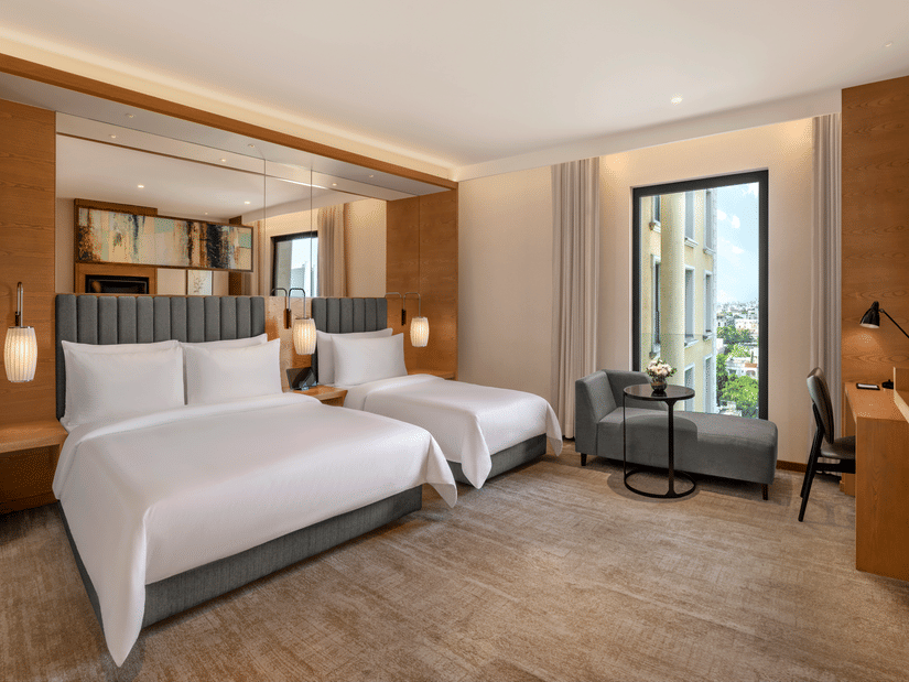 The Suite of Residency Towers, Chennai featuring multiple beds, a wooden flooring, a seating area, a glass window, and overhead lamps.