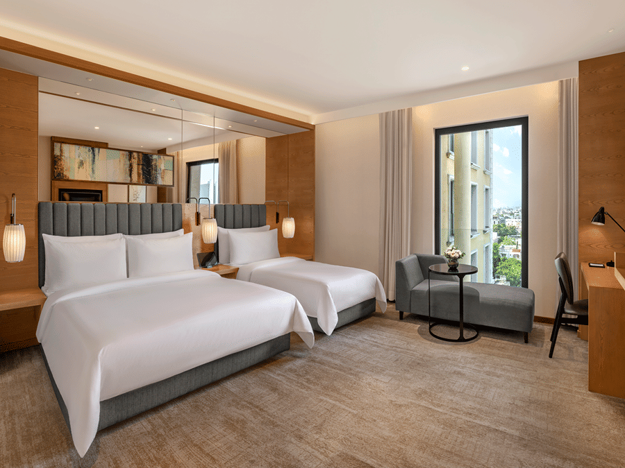The Suite of Residency Towers, Chennai featuring multiple beds, a wooden flooring, a seating area, a glass window, and overhead lamps.