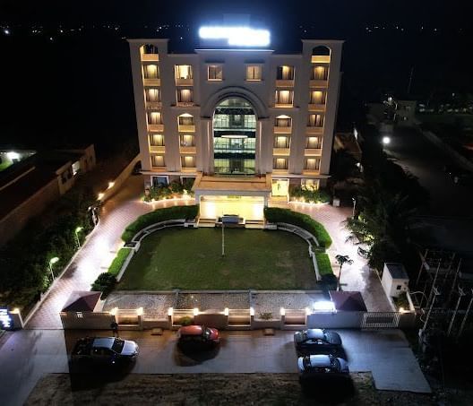 The exterior of a hotel building illuminated at night with a paved pathway and garden | Daksh The Madhuvan Suites