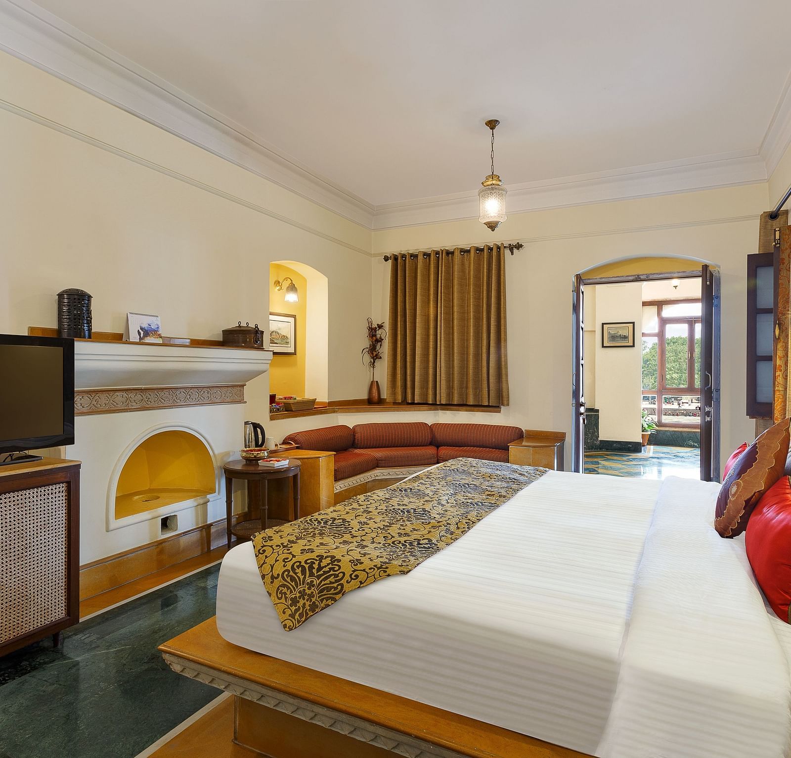 A side view of the suite at The Haveli Hari Ganga in Haridwar showcases its elegant design, featuring a plush bed and stylish furnishings that blend comfort with traditional aesthetics, all set against the backdrop of serene surroundings.