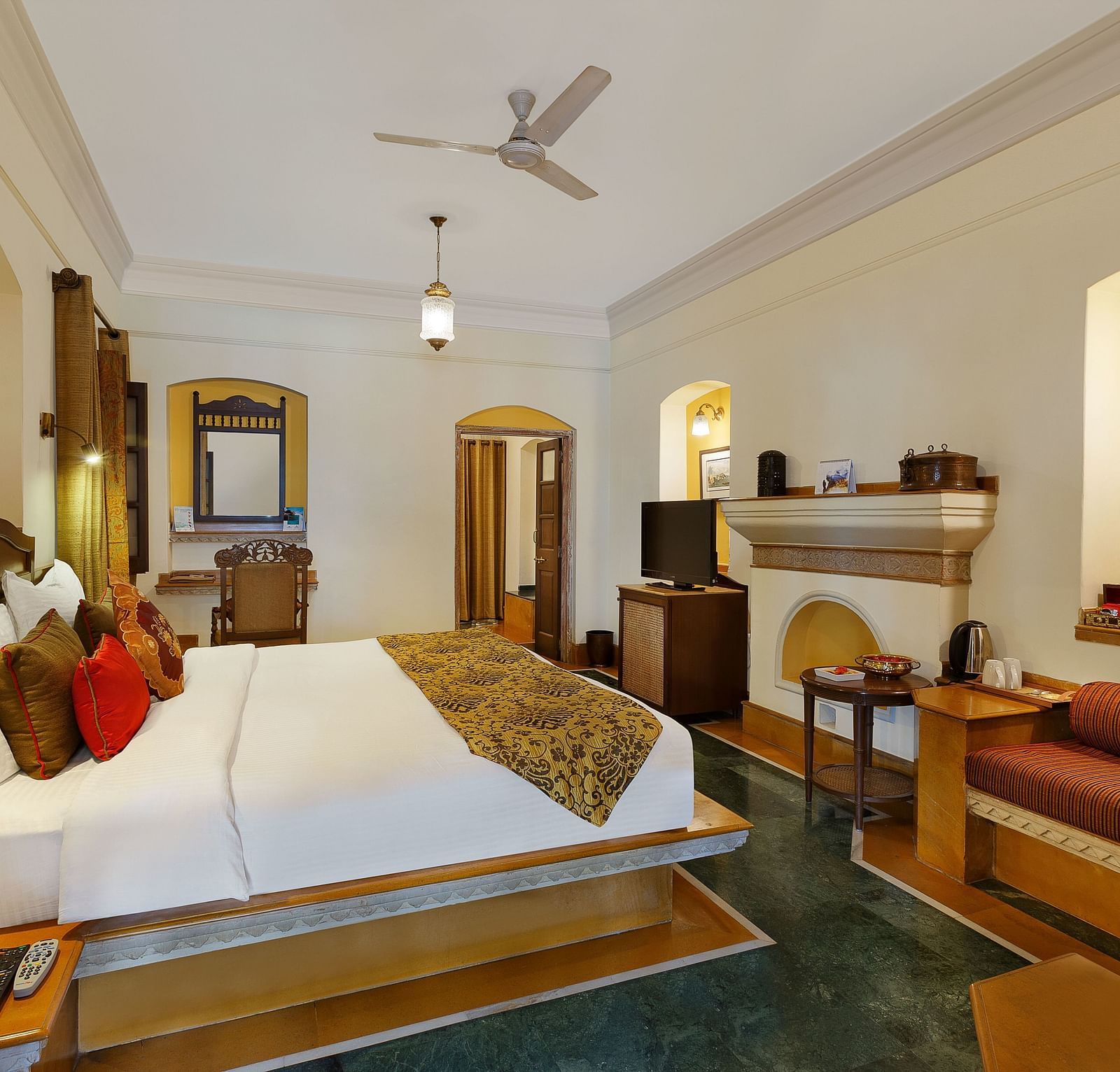A comfy suite at The Haveli Hari Ganga in Haridwar features a plush bed and a diwan, complemented by beautiful interior design that creates a warm and inviting atmosphere for guests.