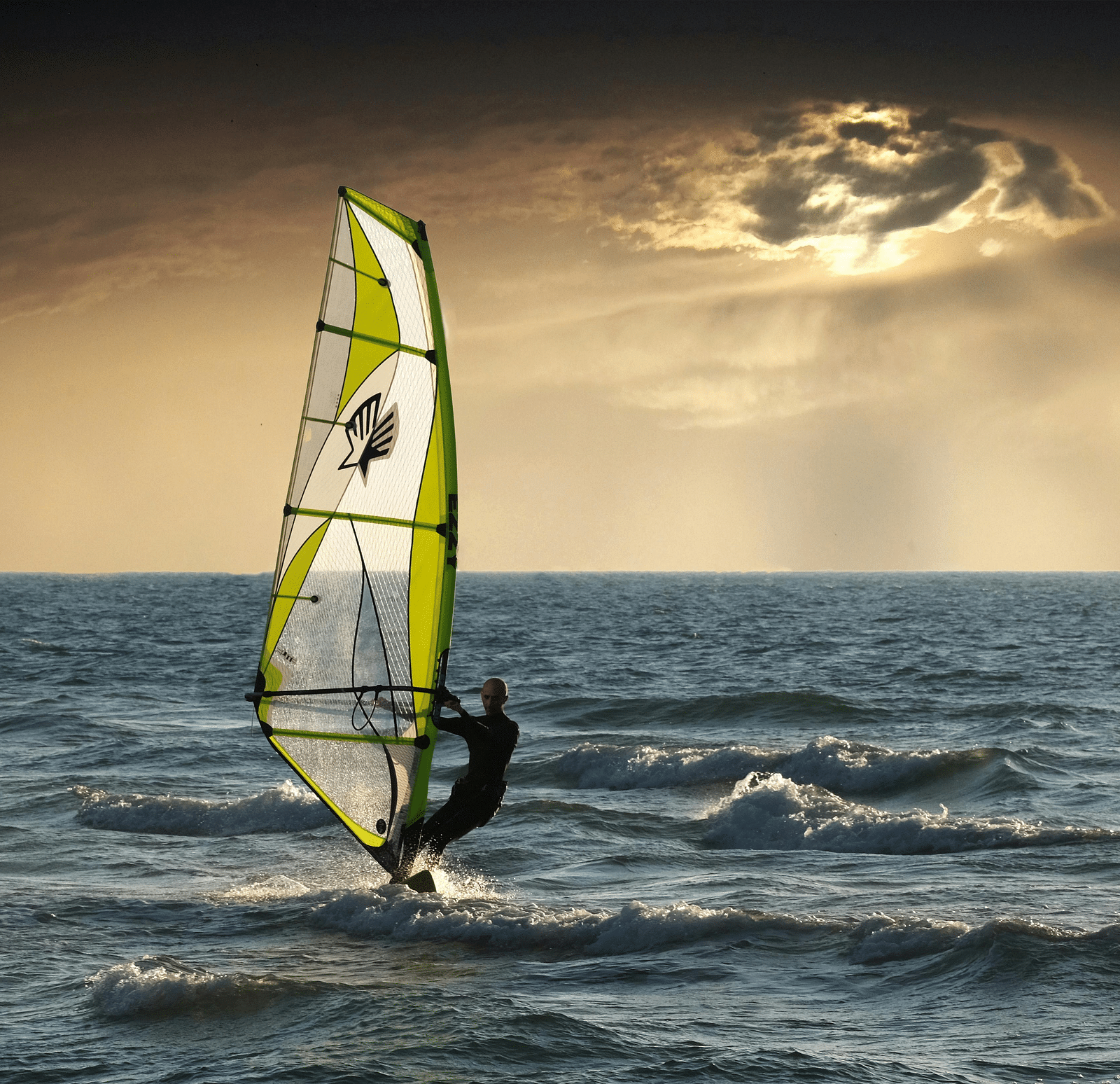 A person windsurfing on the ocean during a cloudy sunset. 