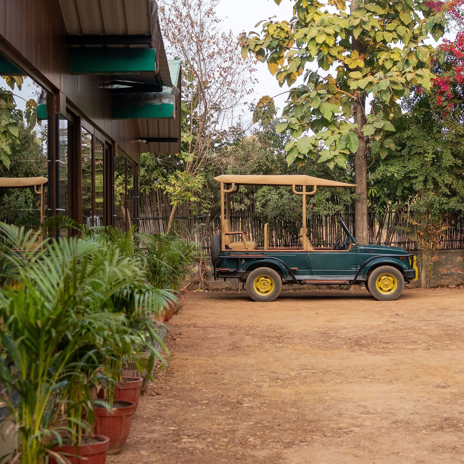 A green safari vehicle parked on a dirt area at Aamaghati Jungle Retreat Ranthambore next to a building.