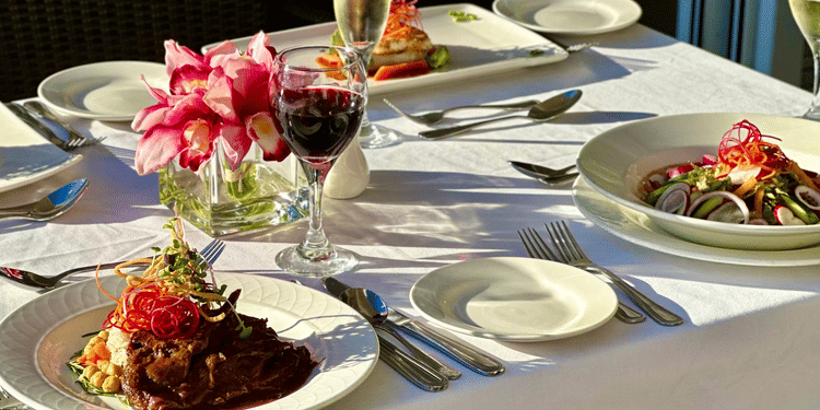 A table set with multiple plated meals, wine glasses, and a flower centerpiece served at The Soco Hotel.