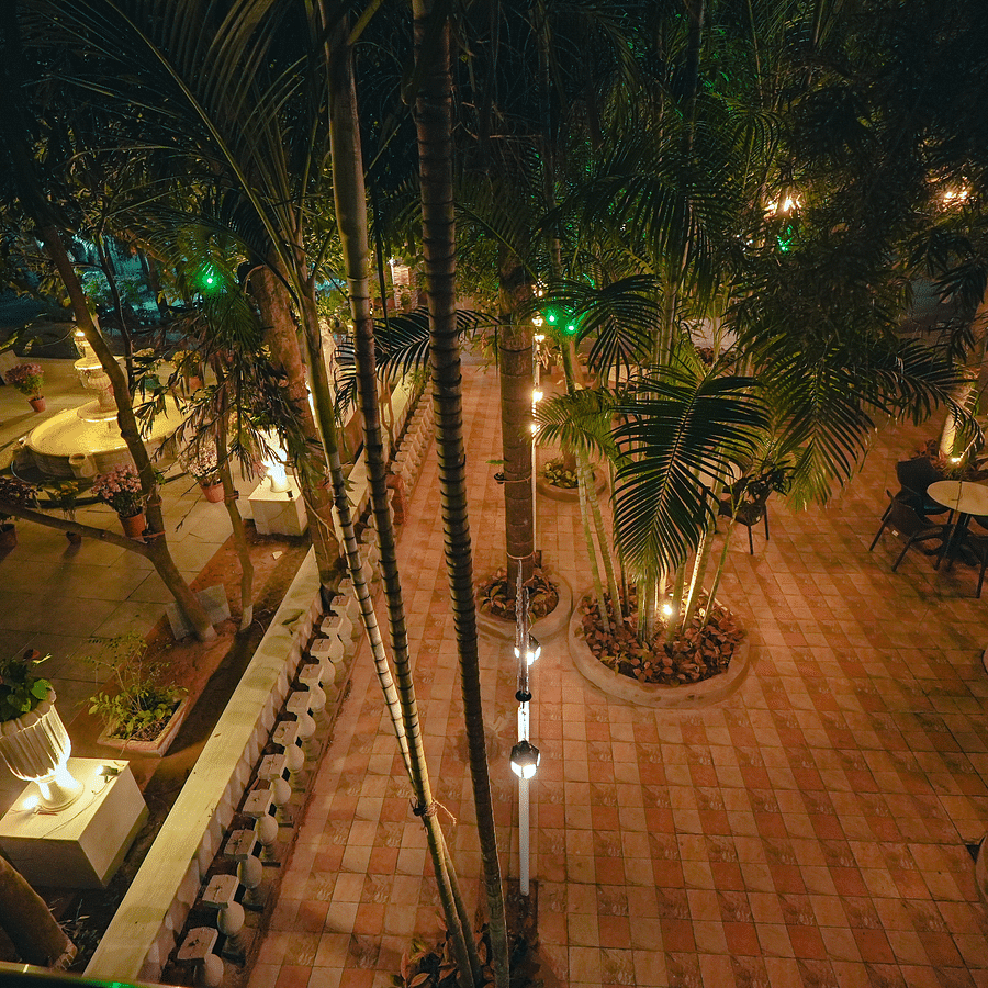 An image of outdoor garden surrounded by trees where tables and chairs are placed at Rangamati Garden Resort