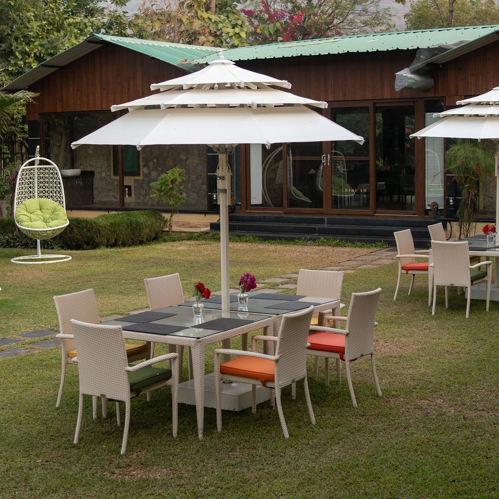 An outdoor seating area at Aamaghati Jungle Retreat Ranthambore with white umbrellas and hanging swing chairs.