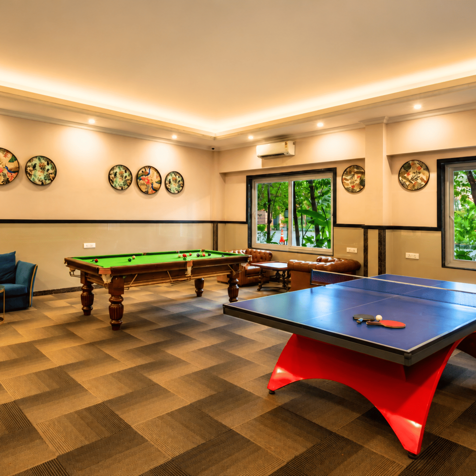 Games room with a billiards table, a table-tennis table, sofas and decorative wall plates beside garden windows at MAYFAIR Oasis Resort & Convention, Jharsuguda.