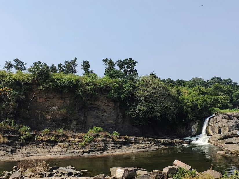 a small waterfall being collected in a waterbody with trees in the background