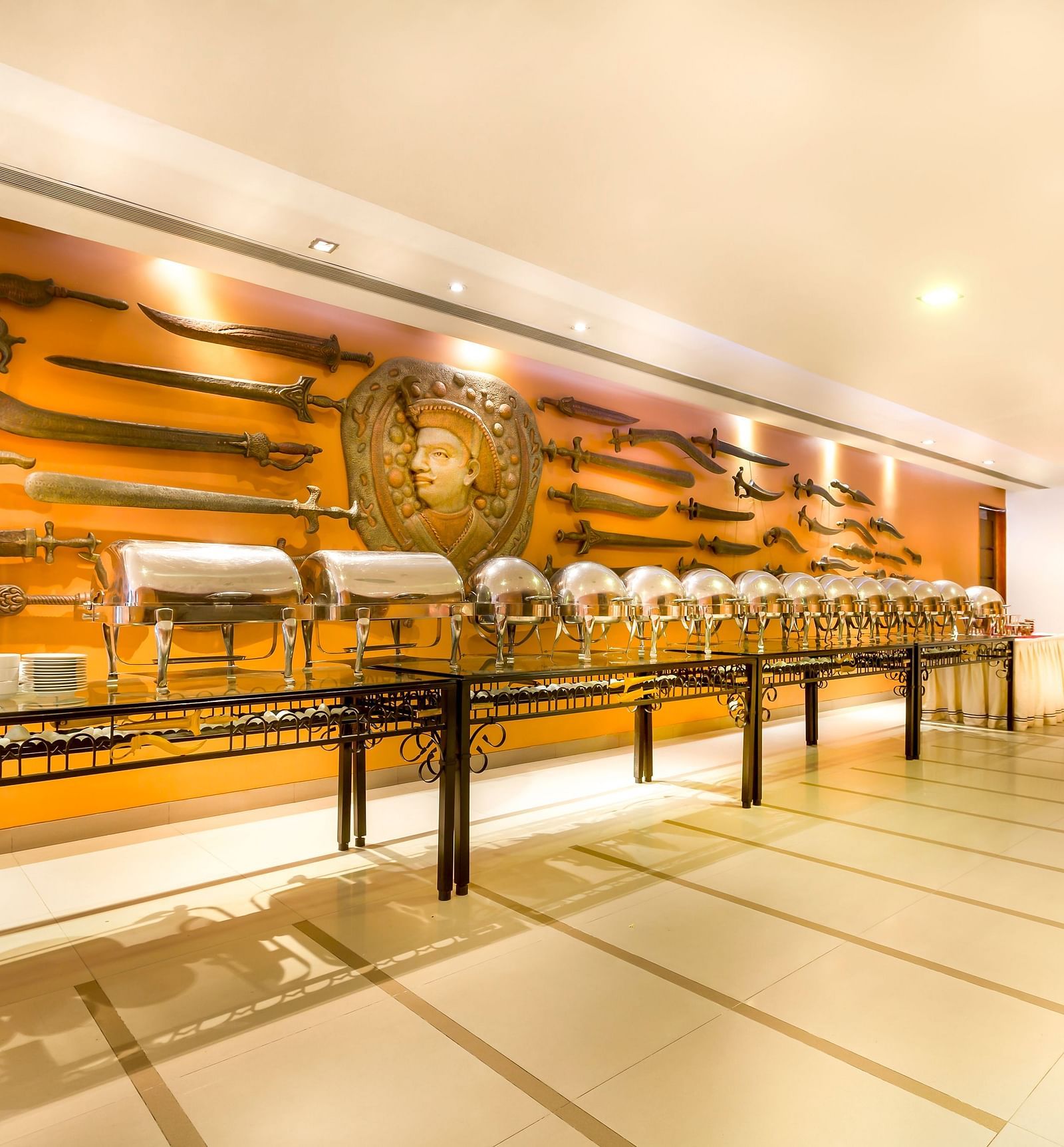 Hotel   with a long buffet table, ornate wall decor featuring swords and shields, and warm lighting.