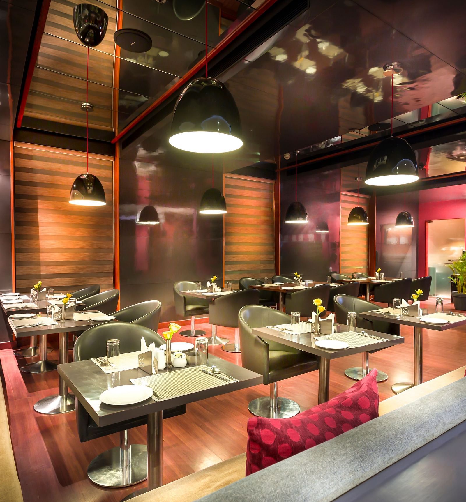 Modern restaurant interior with red accents, plush seating, and a reflective ceiling.