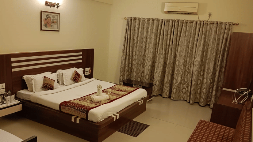Room with king size bed, wooden headboard, bedside lamps, desk, wardrobe, TV, and patterned curtains at Viceroy Beach & Spa Resort, Mandarmani.