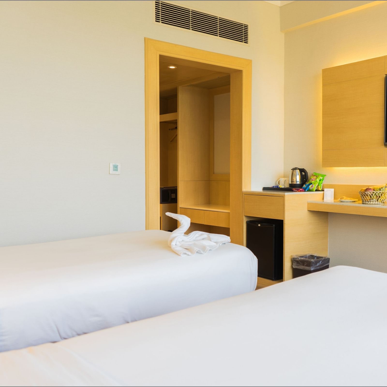 Twin beds with white linens in a room that has a desk and wall-mounted TV | Gemini Continental