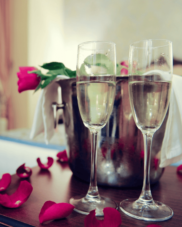 Two champagne flutes and red rose petals are arranged on a bed.