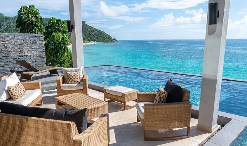 Stylish outdoor lounge area beside an infinity pool, overlooking the turquoise Caribbean Sea and lush hillside of Tamarind Hills.