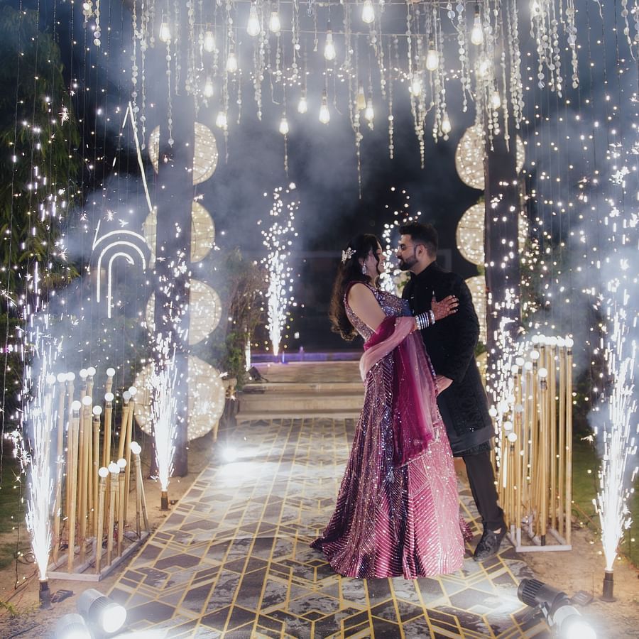 Bride in a magenta lehenga walking under a tunnel of sparklers and string lights during a grand entrance.