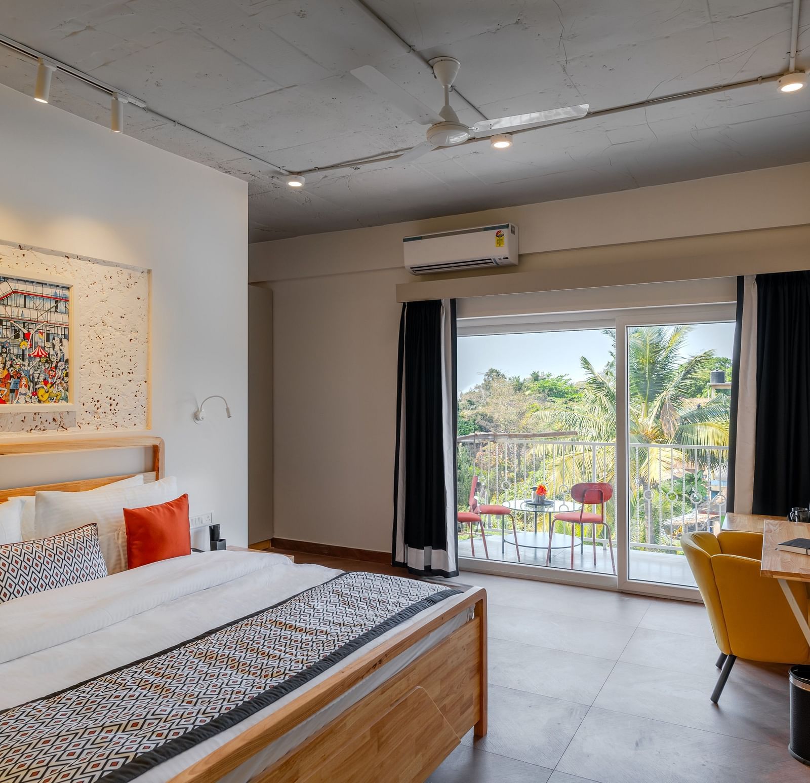 Bright hotel room with, flat TV screen, work desk and chair, vibrant art on the wall, and an access to the balcony at Bedzzz Xclusiv Morjim, Goa