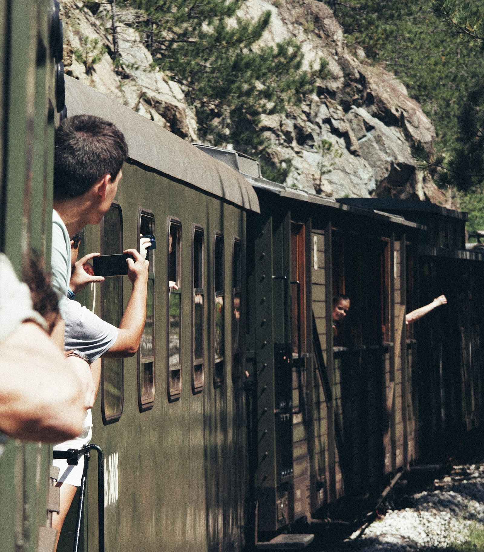 An overview of a train that is travelling on a forest area with people looking out.