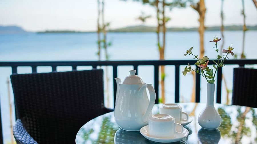 Ceramic water jugs and cups with saucers placed on a glass dining table with the backwaters at Coorg Jungle Camp Backwater Resort, Kushalnagar in the backdrop.