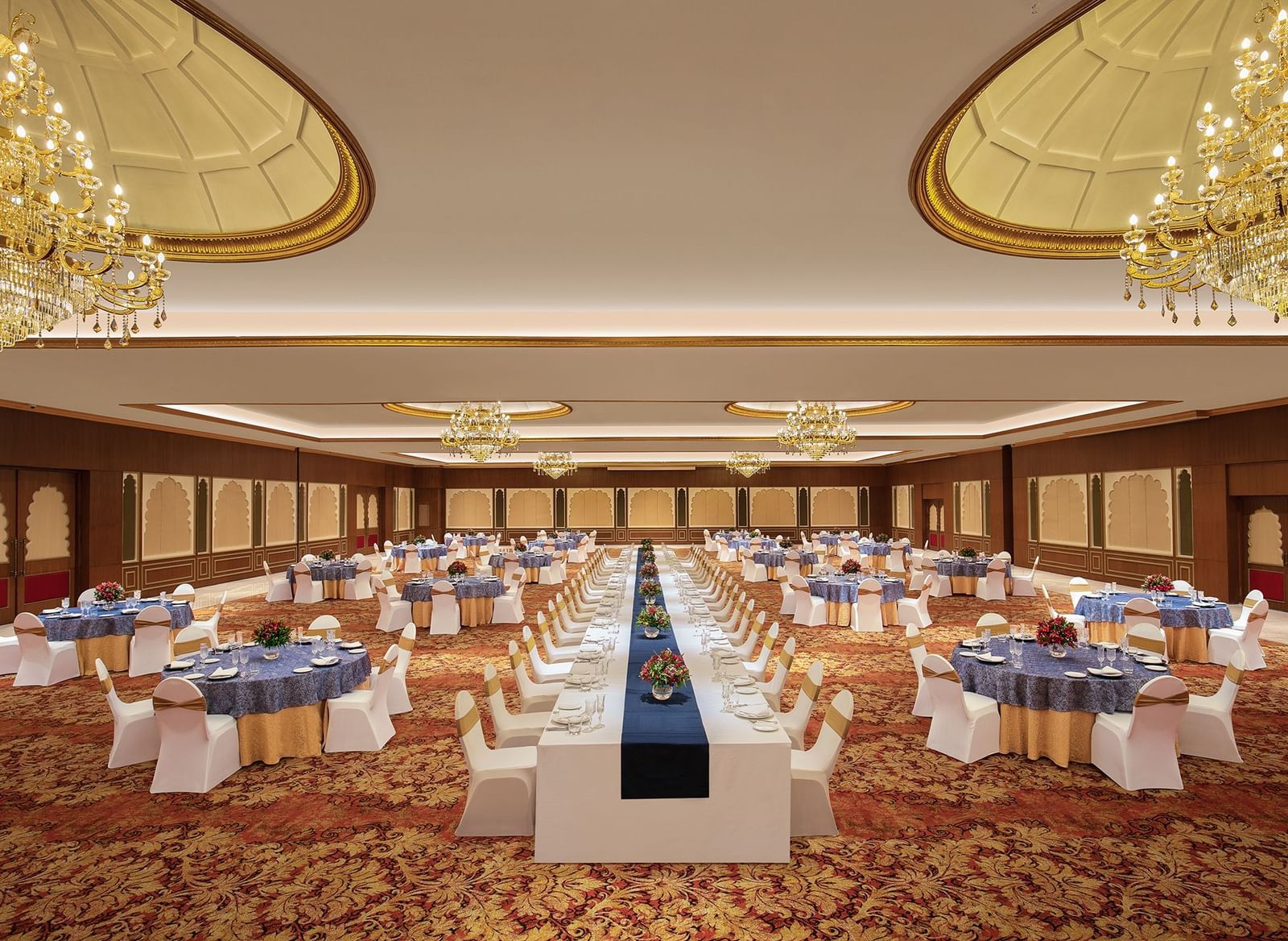 An image of a cosy event hall in Mahabalipuram with long and round tables, chandeliers, and carpeted floors – Kaldan Samudra Palace, a Luxury Wedding Hall in ECR