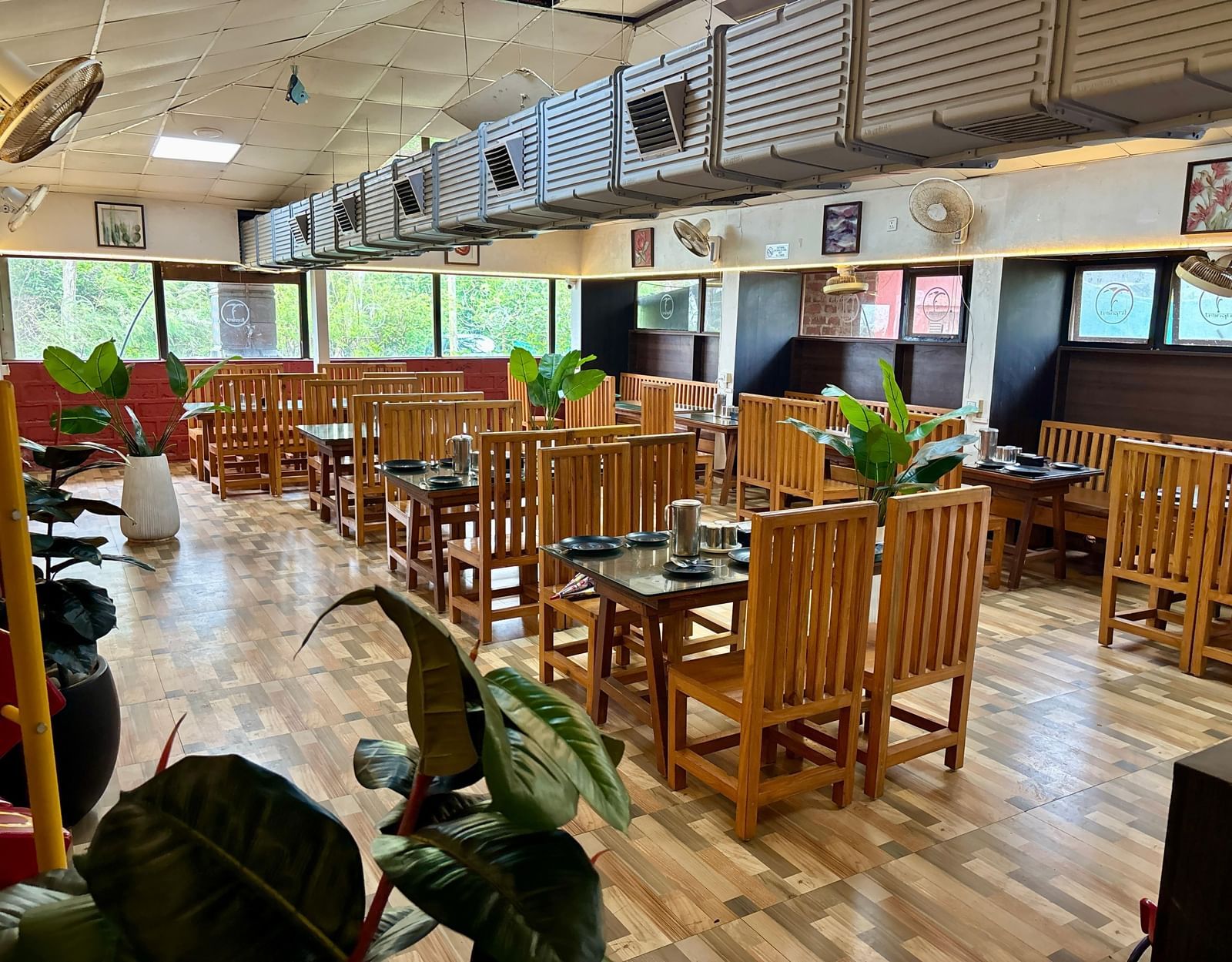 An empty dining area with simple wooden tables and chairs, and large potted plants placed throughout the room - Tranquil Beach Resort, Harihareshwar