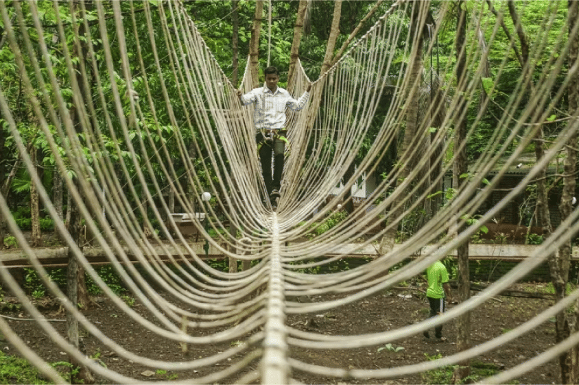 A guest walks through Burma Bridge at Sajan Nature Club in a natural outdoor setting.