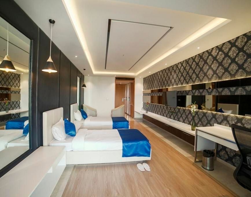  spacious hotel room at BNGV Grandeur Hotel and Banquets, with a long perspective showcasing the bed, a desk area, and modern architectural lines.