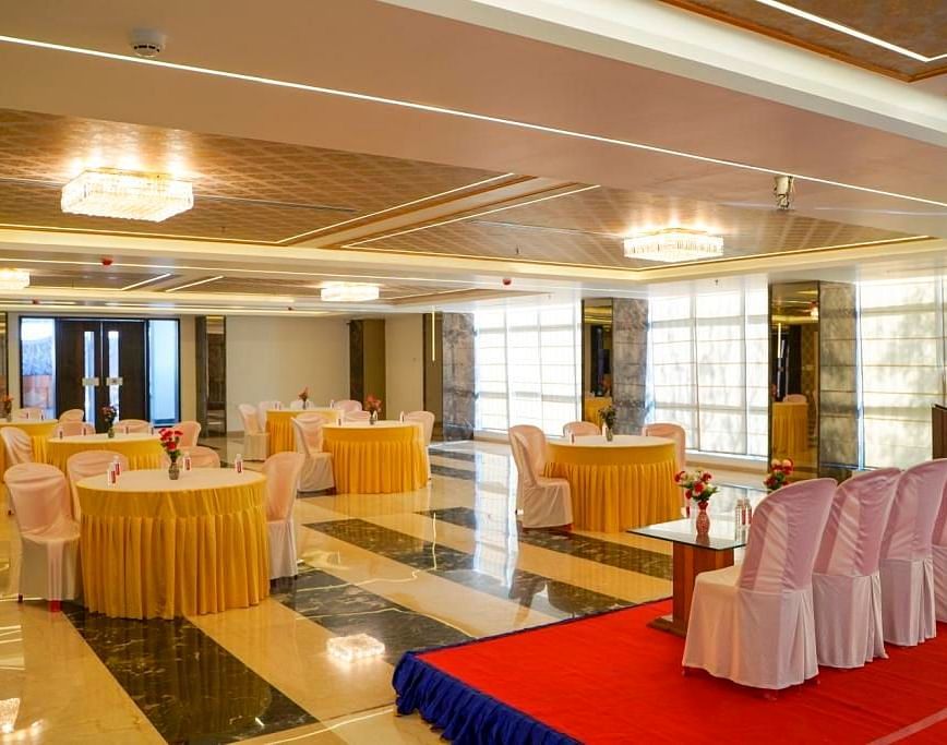 A grand banquet hall at BNGV Grandeur Hotel and Banquets with round tables, a red stage, and elegant lighting, set for an event.