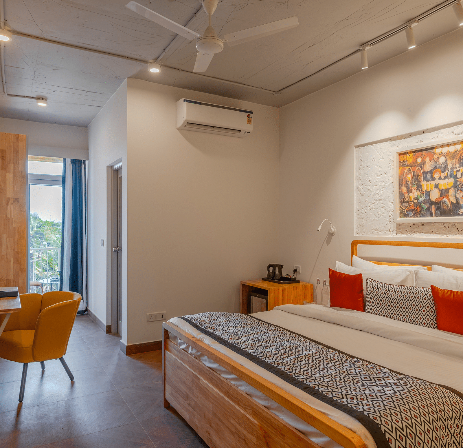 Bright hotel room with, flat TV screen, work desk and chair, vibrant art on the wall, and an access to the balcony at Bedzzz Xclusiv Morjim, Goa