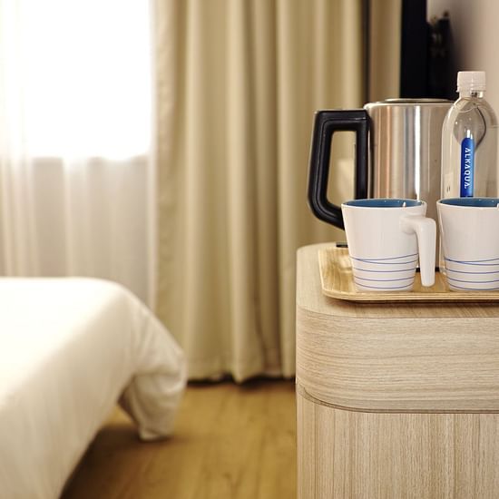 An electric kettle and mugs set on a coffee table across a bed