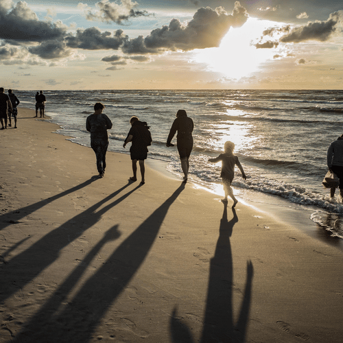  A family walking along a sandy beach at sunset, casting long shadows on the ground next to ocean waves.