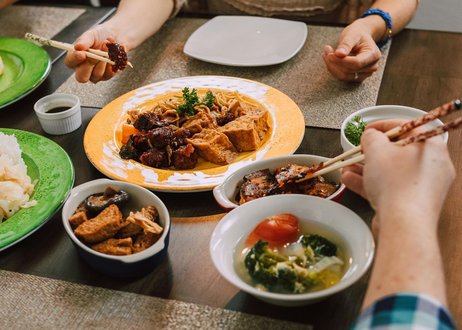 two people dining together each holding a pair of chopsticks with various Asian cuisine served on the table